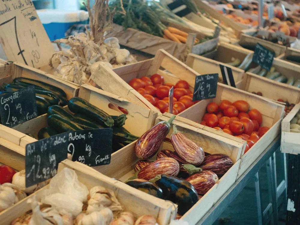 Wooden crates of tomatoes, courgettes, aubergines and garlic on a market stall.