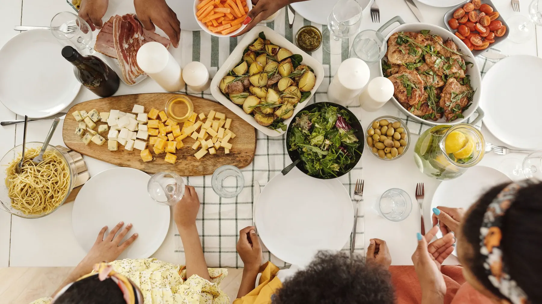 An overhead view of a table with several dishes on it and several people reaching across it.
